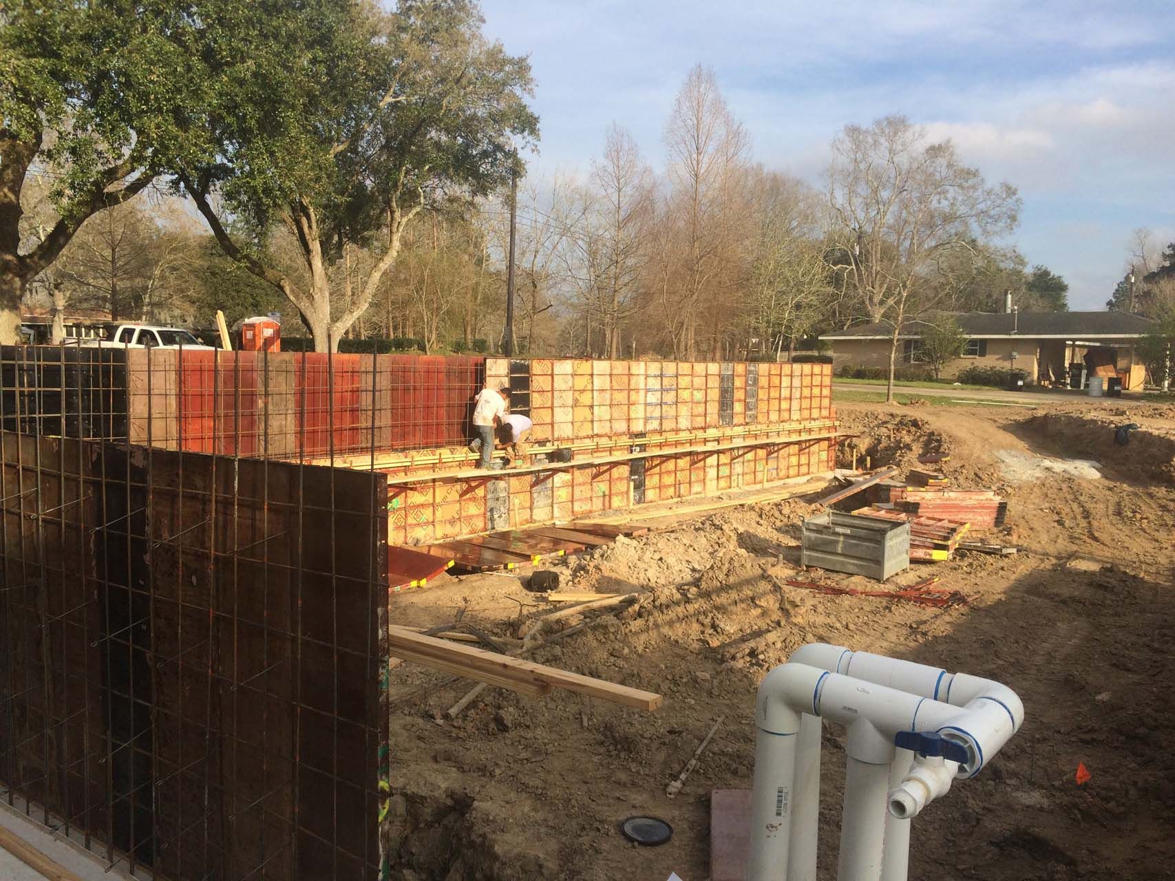 Construction site with wooden forms for concrete walls. A worker stands inside the forms.