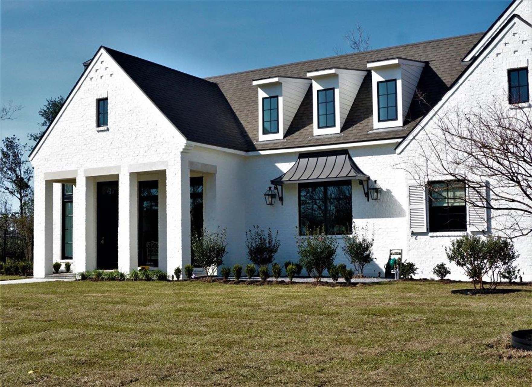White stucco house with dark roof, windows, and awning; green lawn.