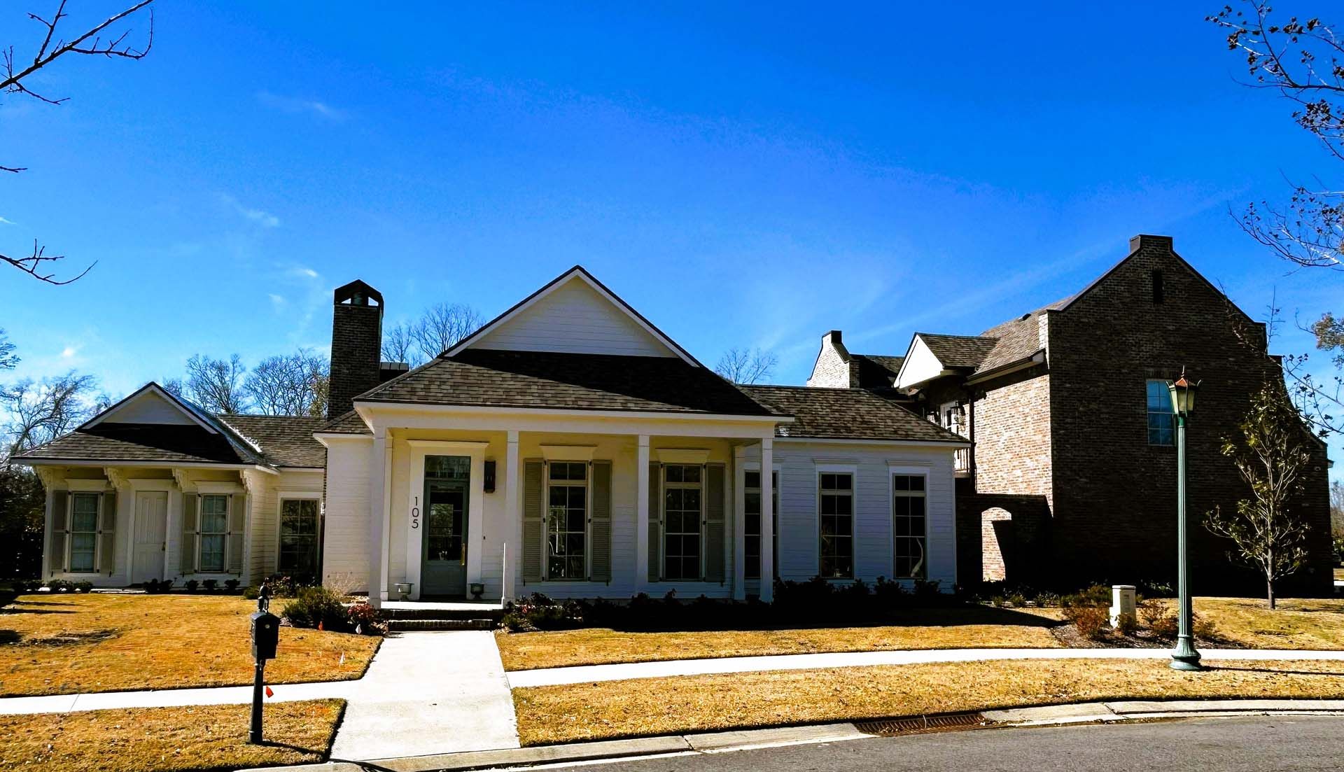 White house with a gabled roof and front porch on a sunny day. A brick structure is attached.