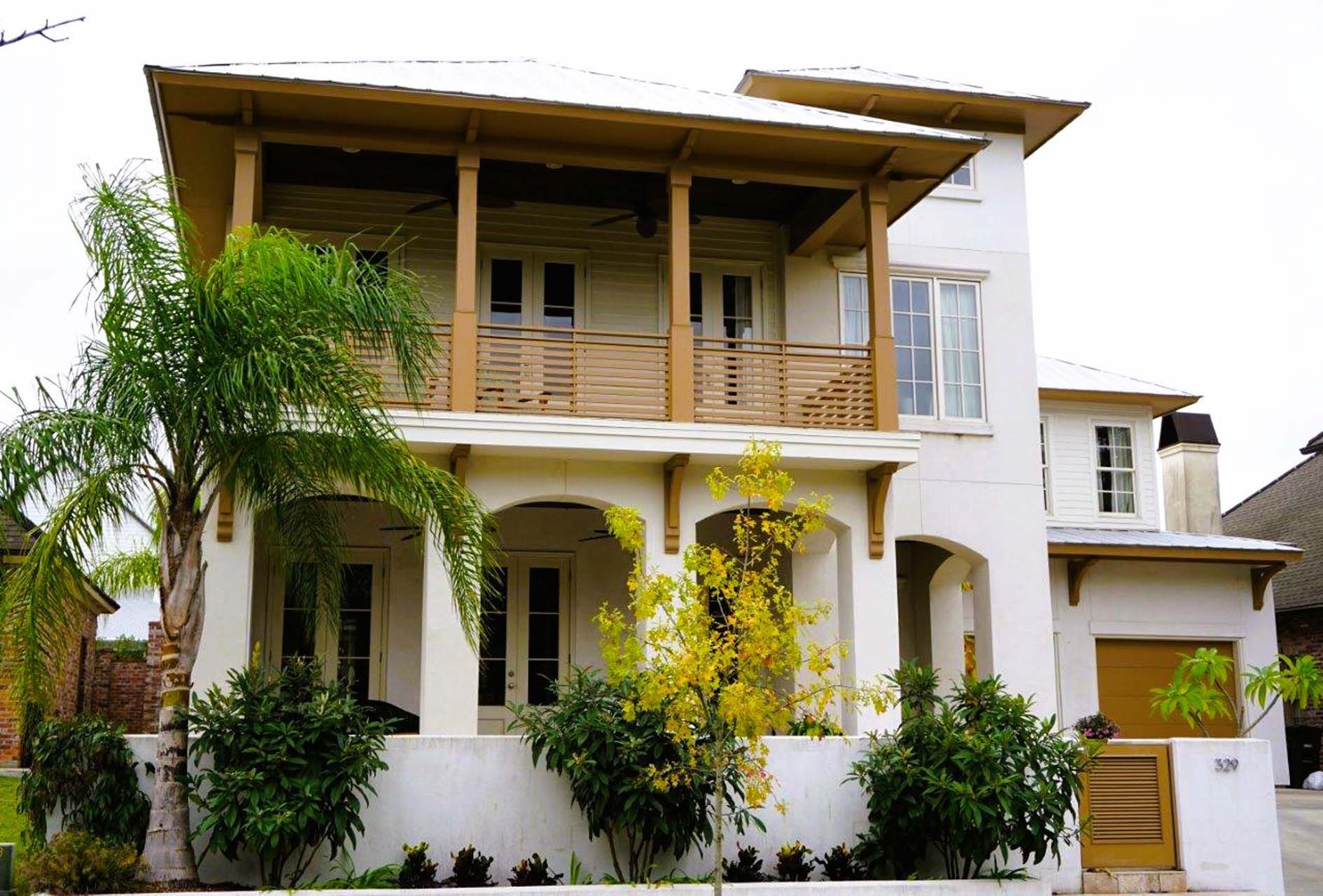 White multi-story house with wooden balconies and trim, and lush landscaping.