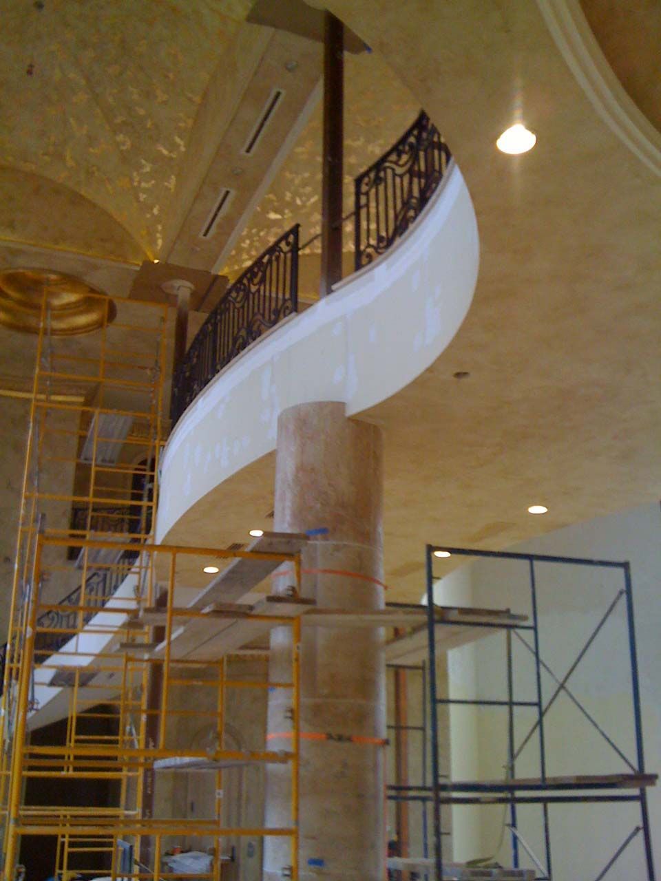 A curved, unfinished staircase winds around a tall column; scaffolding surrounds it.