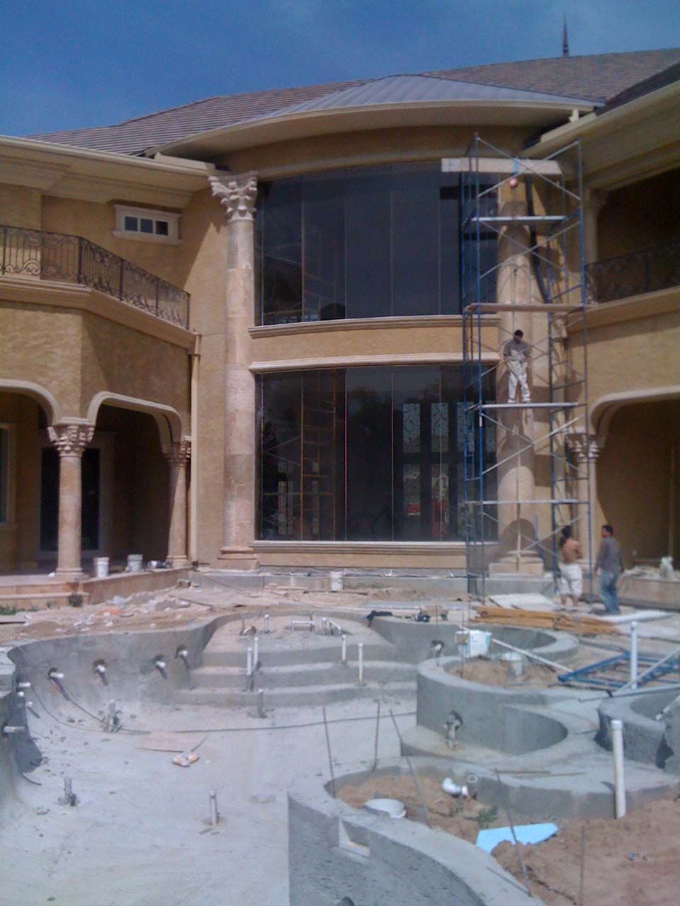 A large house under construction with scaffolding, workers, and a partly built pool.