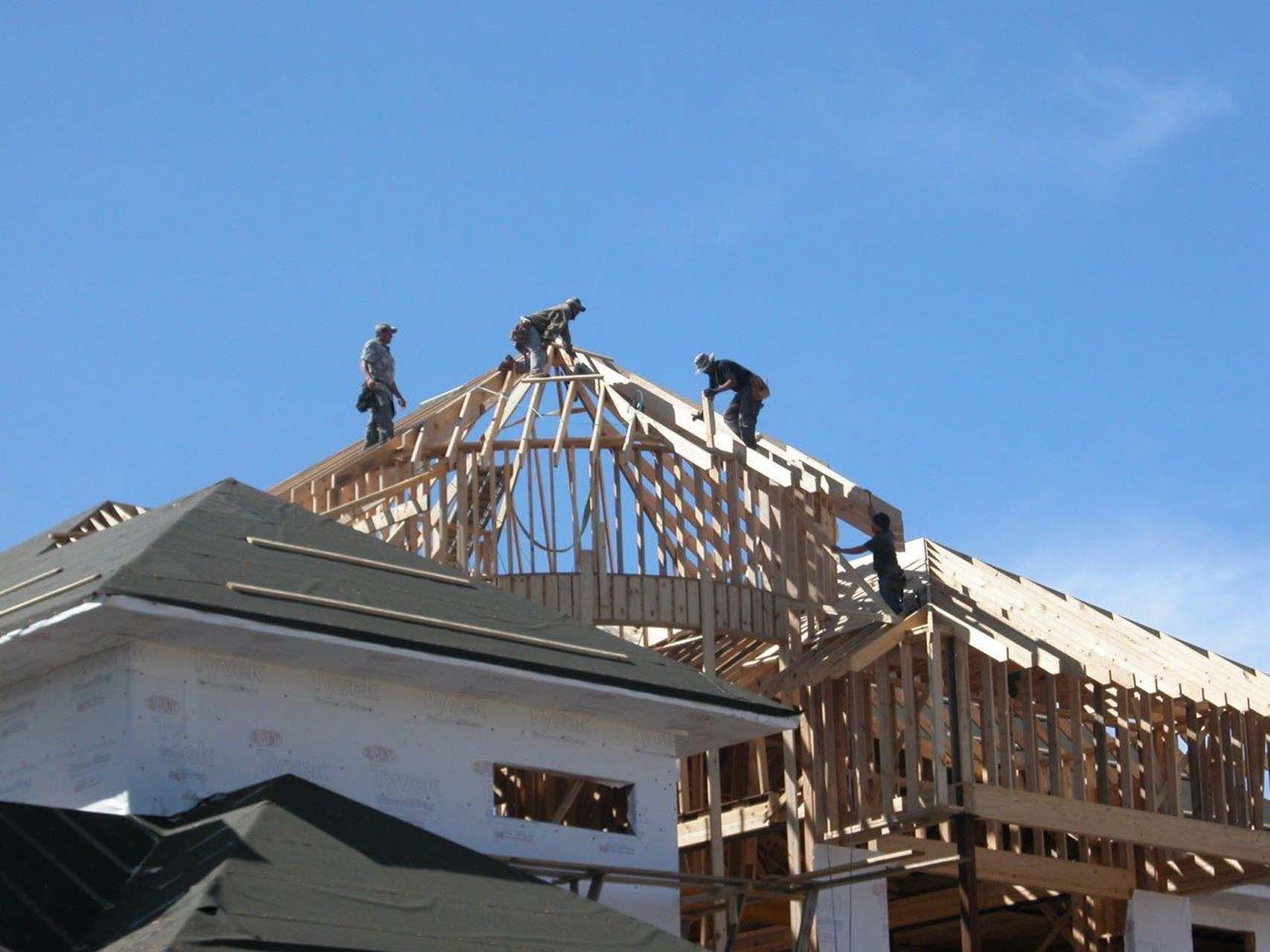 Construction workers building a wooden roof frame on a house under a clear blue sky.