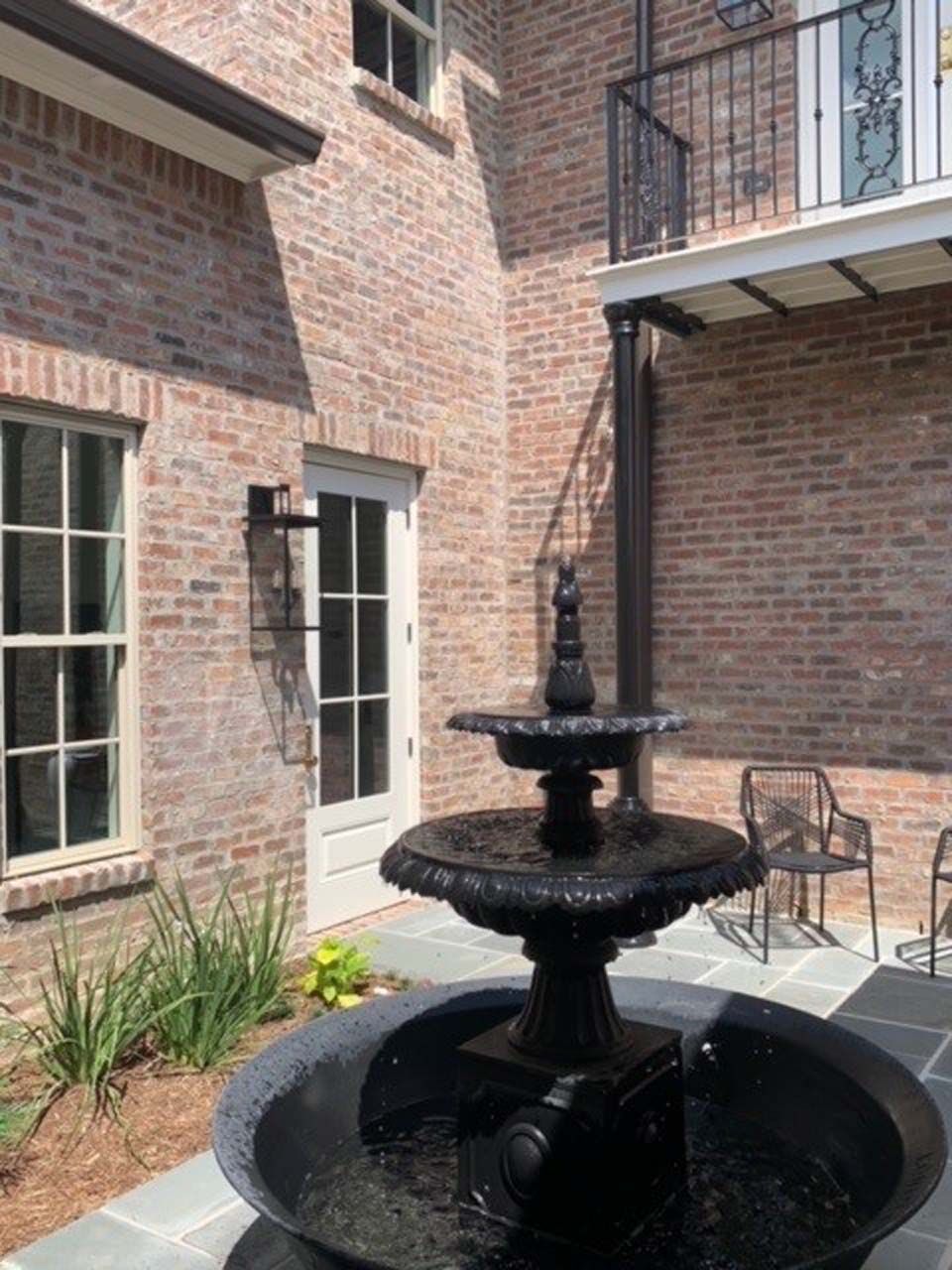Brick courtyard with a black fountain and a balcony.