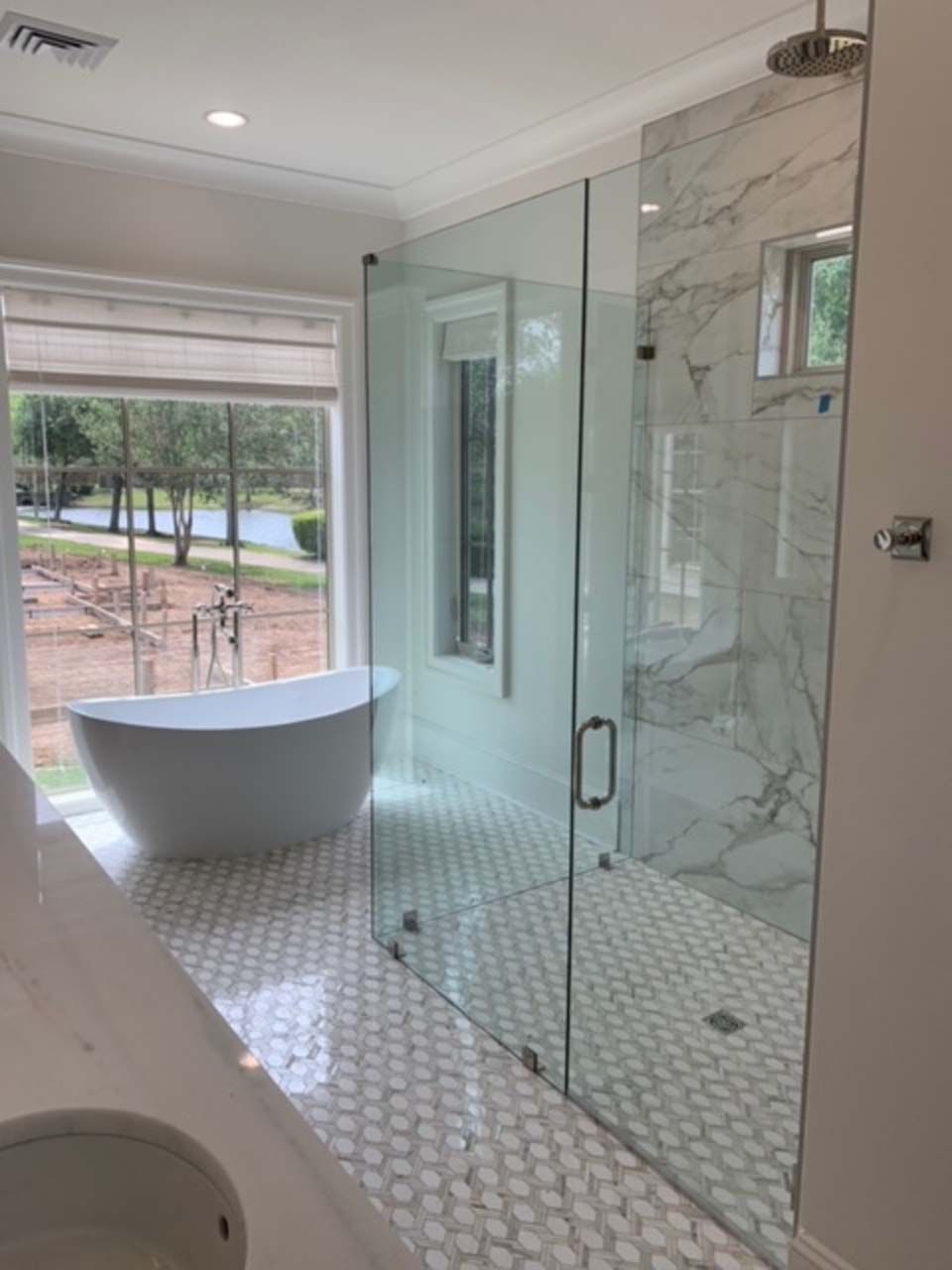 Modern bathroom with white tub, marble shower, and glass door.