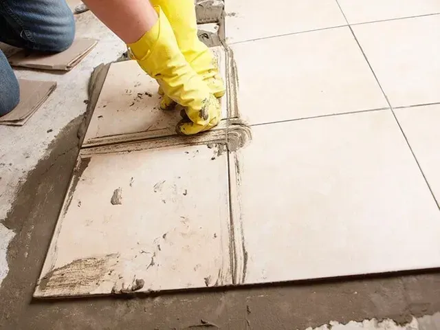 Una persona que lleva guantes amarillos está colocando baldosas en el suelo.