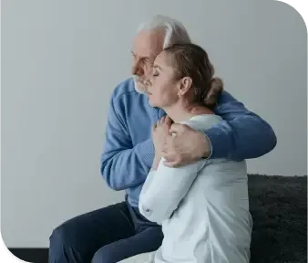Older man hugging a woman seated beside him in a plain studio setting