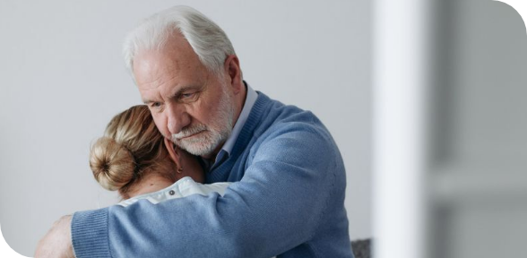 Two people embrace in a comforting hug, with one in a blue shirt holding the other closely indoors.