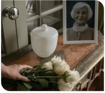 White roses beside an urn and framed portrait on a memorial table