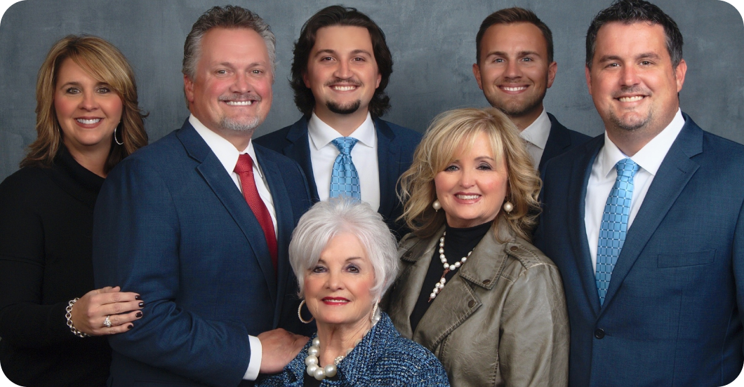 Seven people pose in formal business attire against a dark studio backdrop.