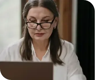 Woman in glasses looking down at a laptop in a bright office setting
