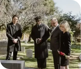 Four mourners in black stand solemnly at a graveside in a cemetery.