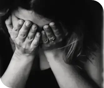 Person sitting with face covered by both hands, appearing distressed in black and white.