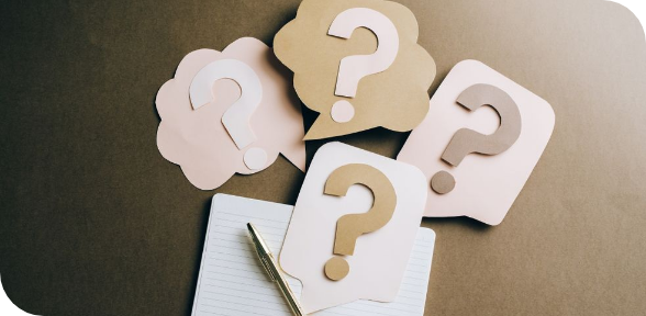 Paper question marks over a notebook with a pen on a dark surface
