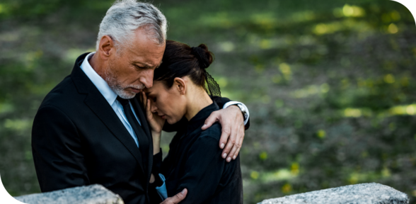 Two people embracing outdoors, resting their foreheads together in a somber moment