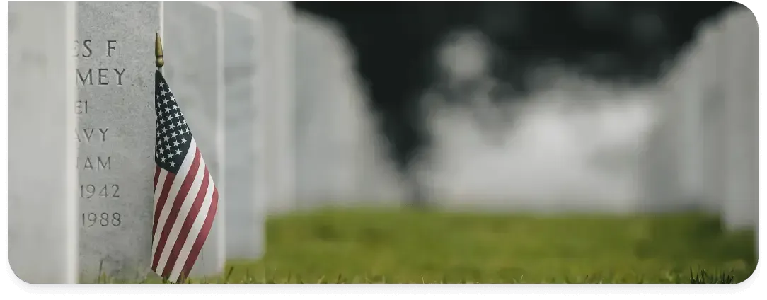 American flag beside a gravestone in a cemetery, with a blurred green background