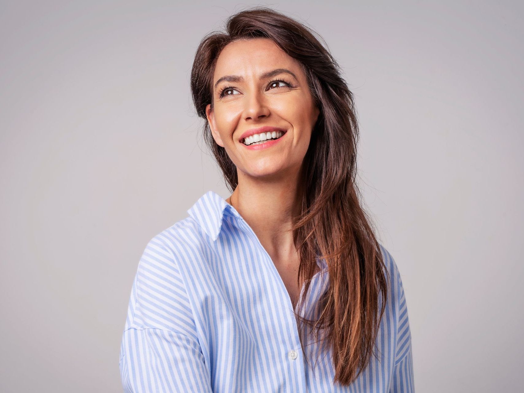 A woman in a blue striped shirt is smiling and looking up