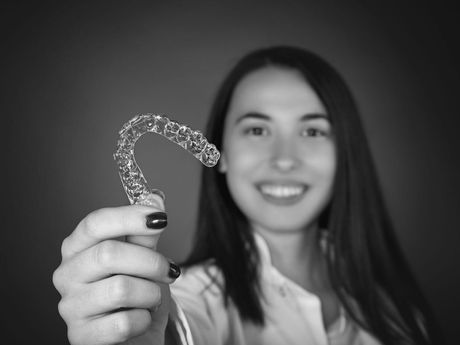 A woman is smiling and holding a clear brace on her teeth