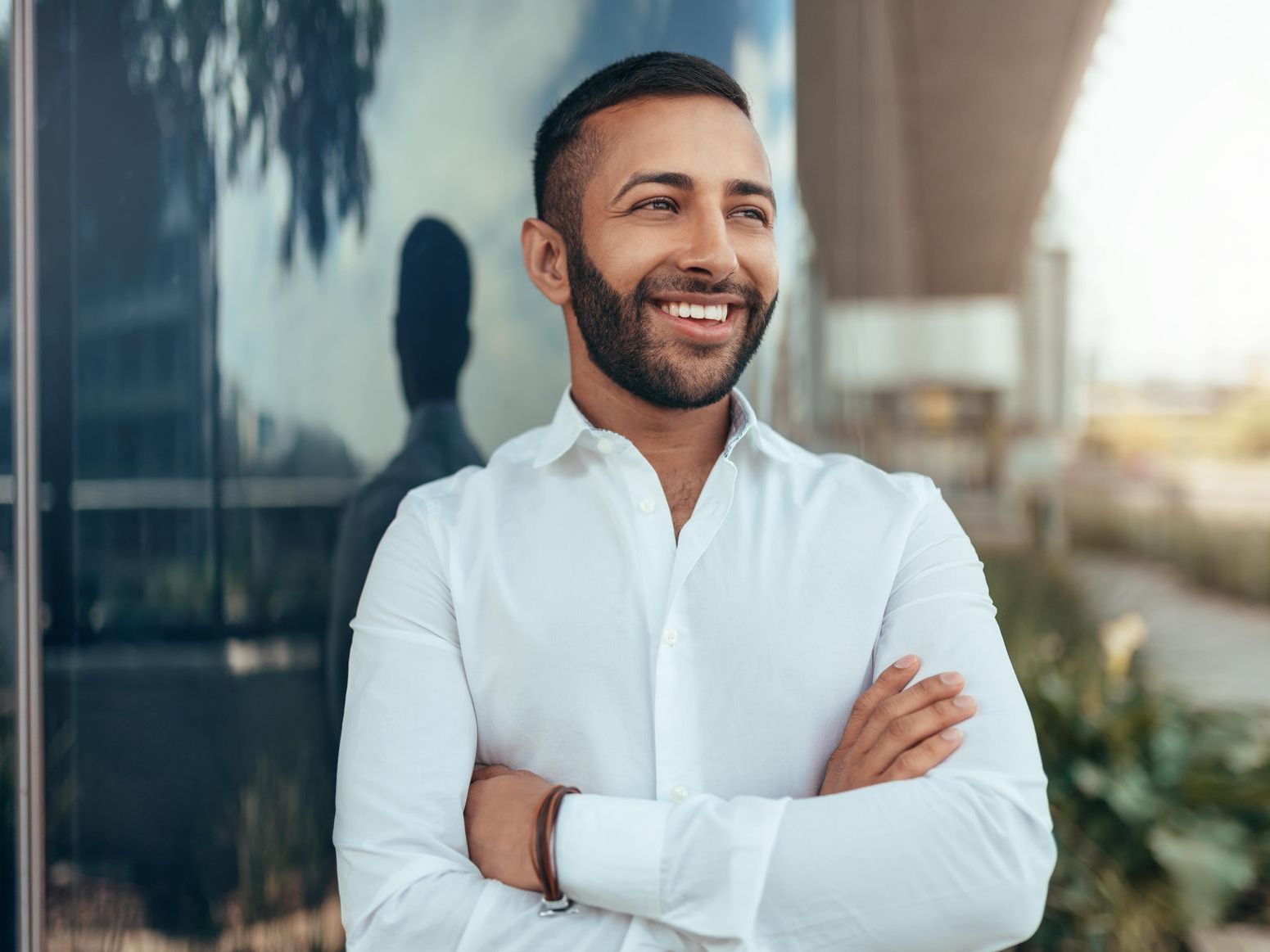 A man in a white shirt is standing with his arms crossed and smiling