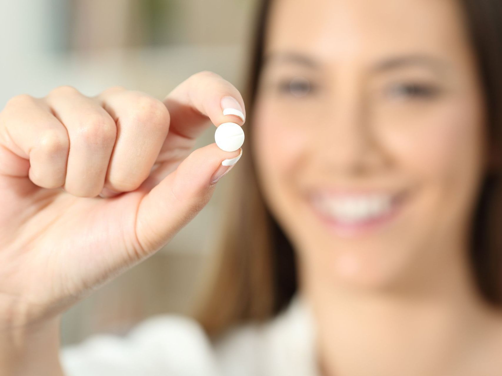 A woman is holding a pill in her hand and smiling