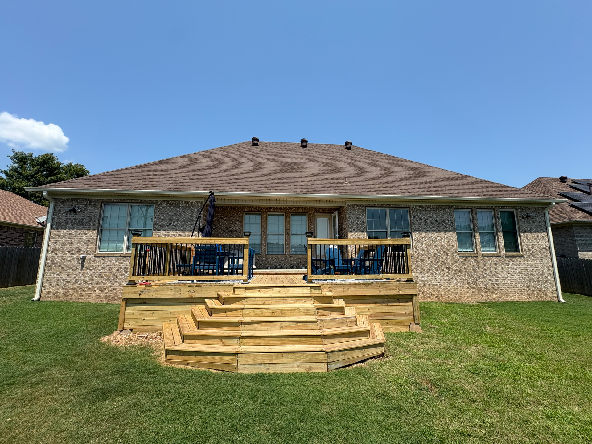 A brick house with a newly constructed wooden deck featuring wide, terraced stairs leading into a grassy backyard.