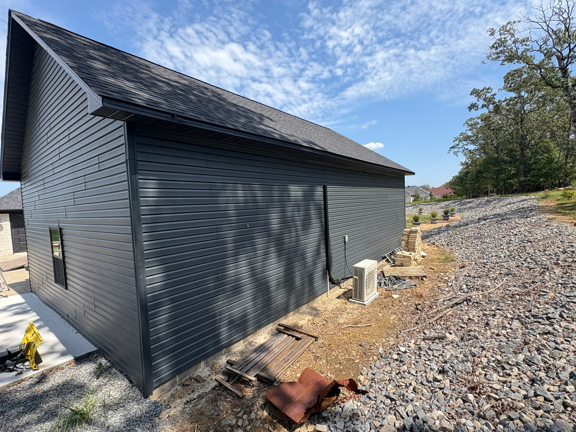 A side view of a modern house with black horizontal siding and a dark gabled roof, set against a rocky hillside.