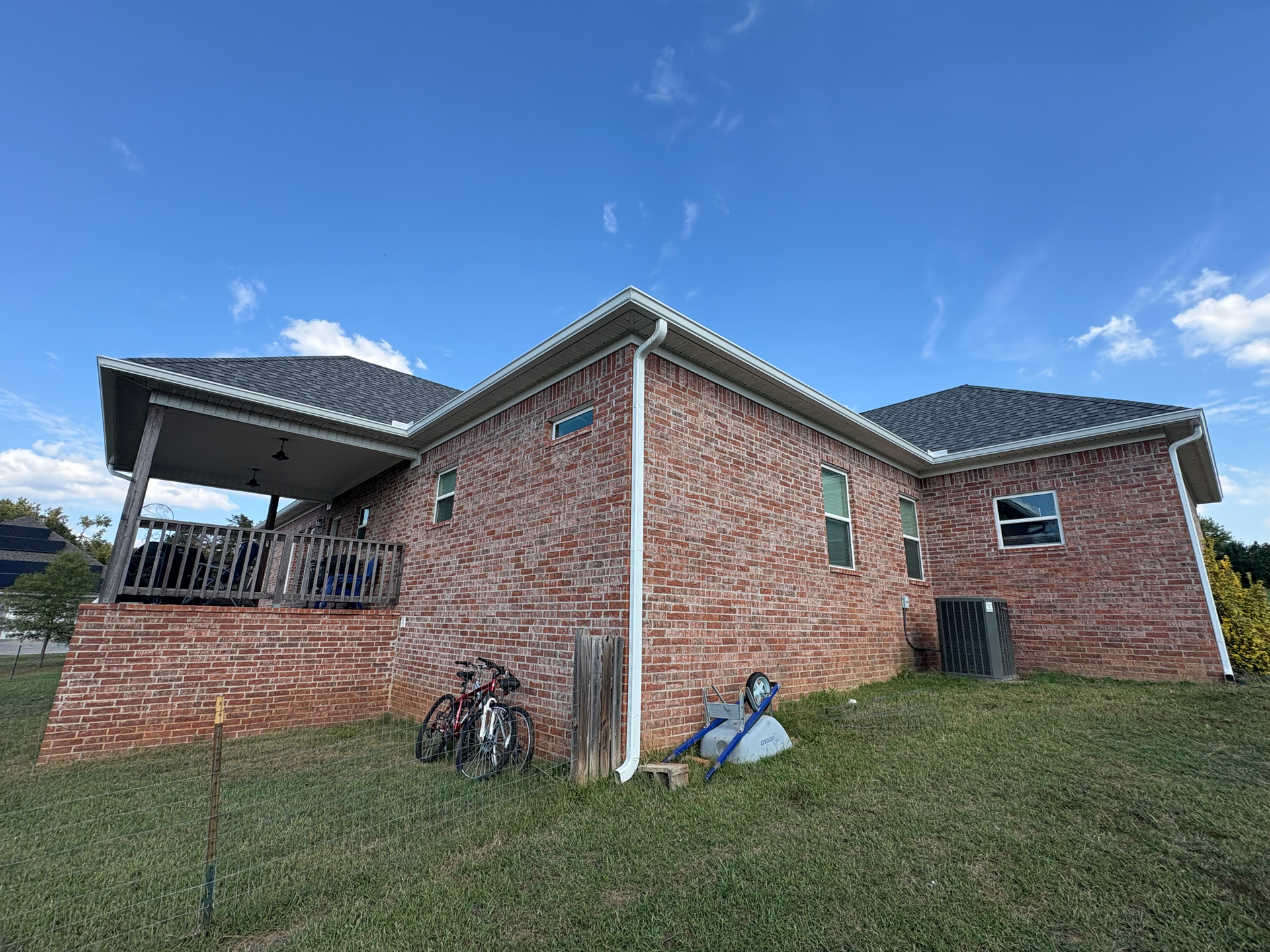 A brick ranch-style house with a covered back patio, a lawn, two bicycles, and a blue sunny sky.