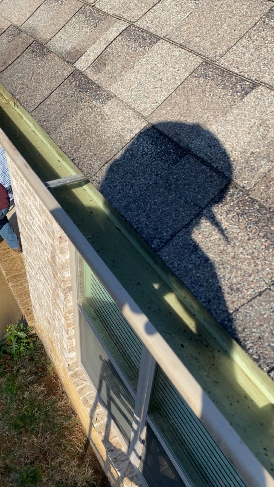 A person's shadow cast onto shingles near a house gutter and downspout.