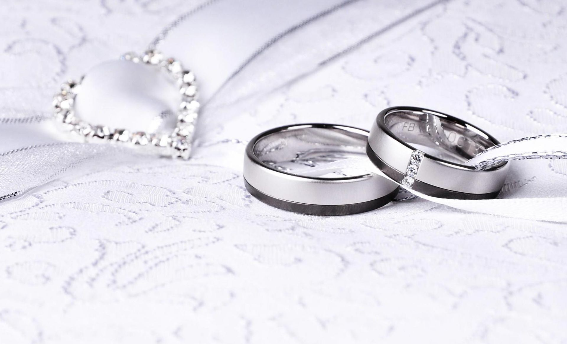 A pair of wedding rings and a necklace are on a white cloth.