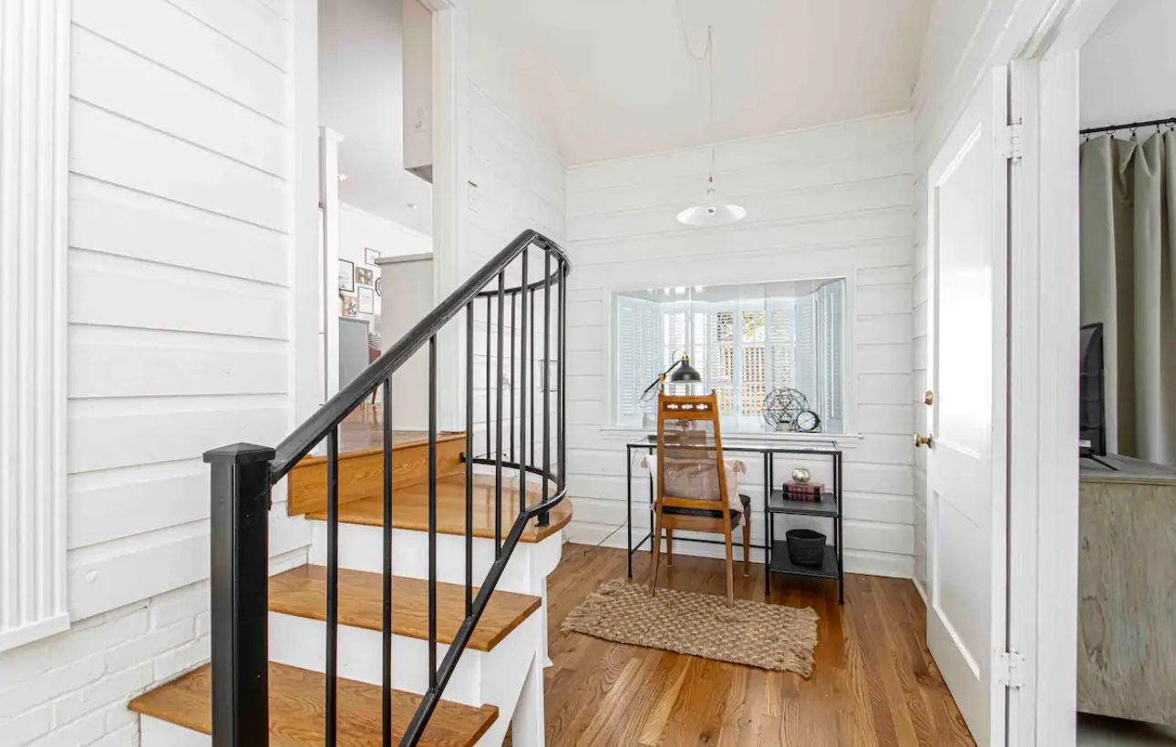 Hallway with stairs and desk area; white paneling, black railing, wood floors.