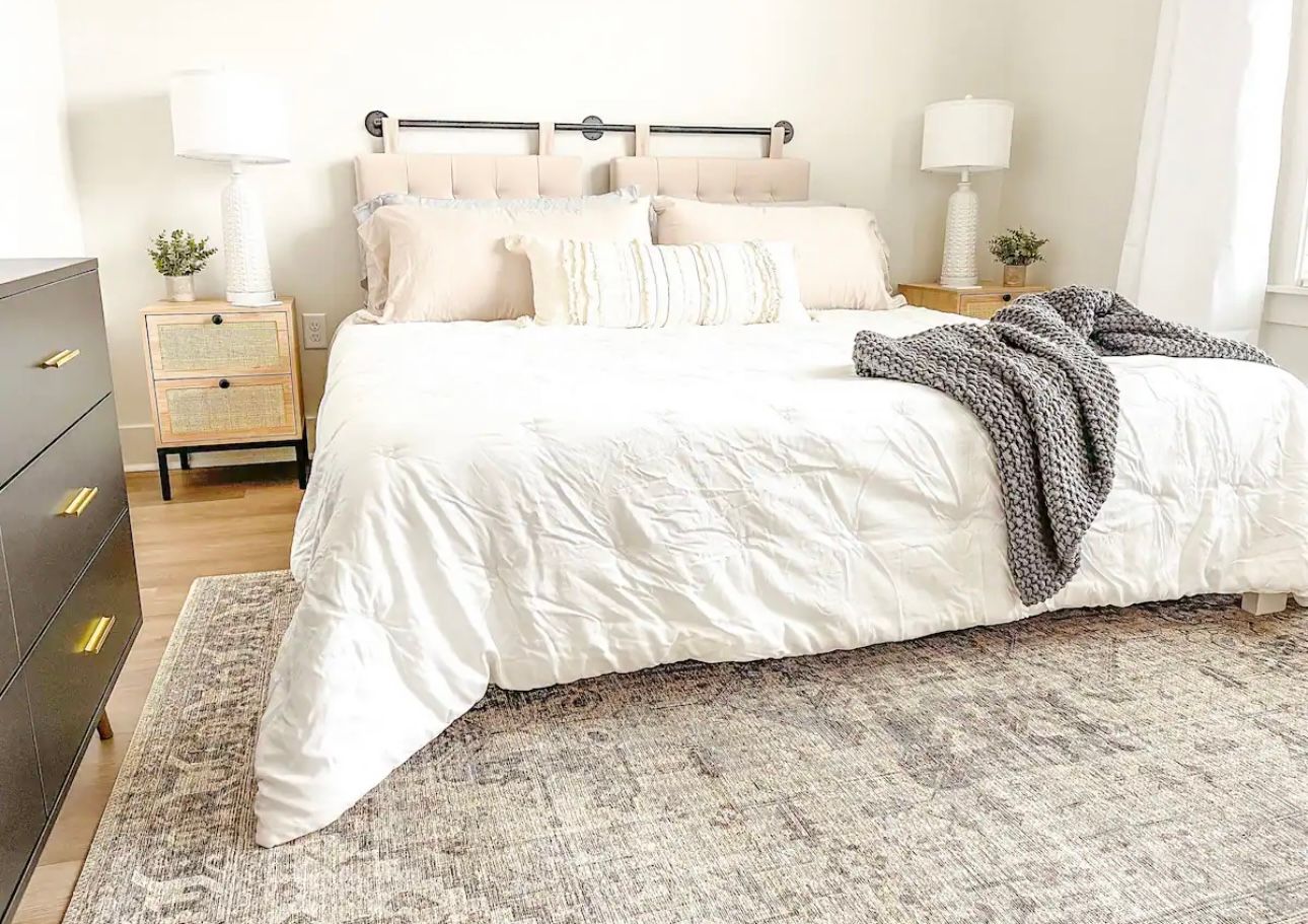 Bedroom with bed, nightstands, and rug. White bedding, gray blanket, neutral decor.