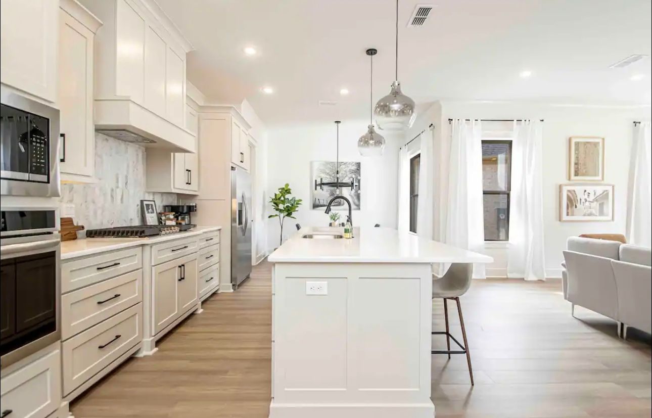 Bright white kitchen with island, stainless steel appliances, and wood floors.