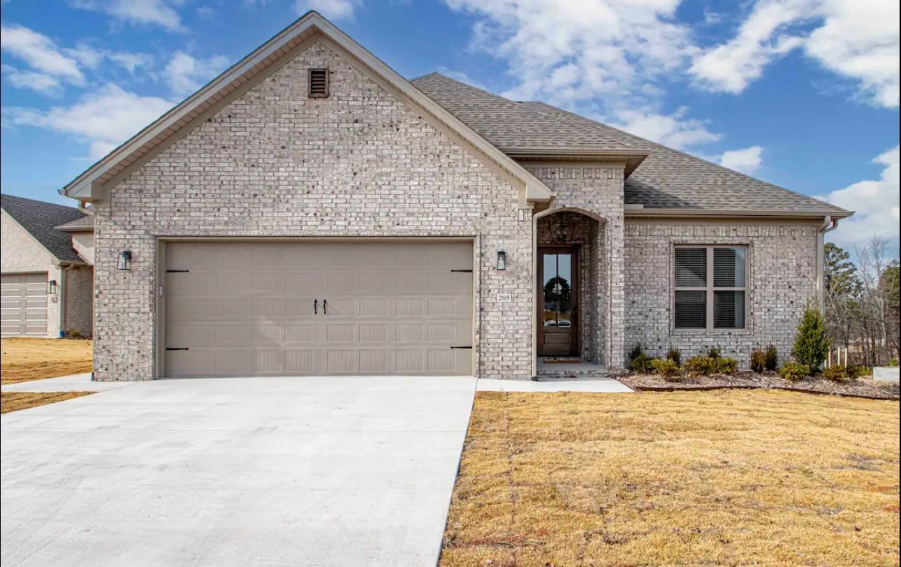 Single-story brick house with attached garage, arched entry, and dry landscaping under a partly cloudy sky.