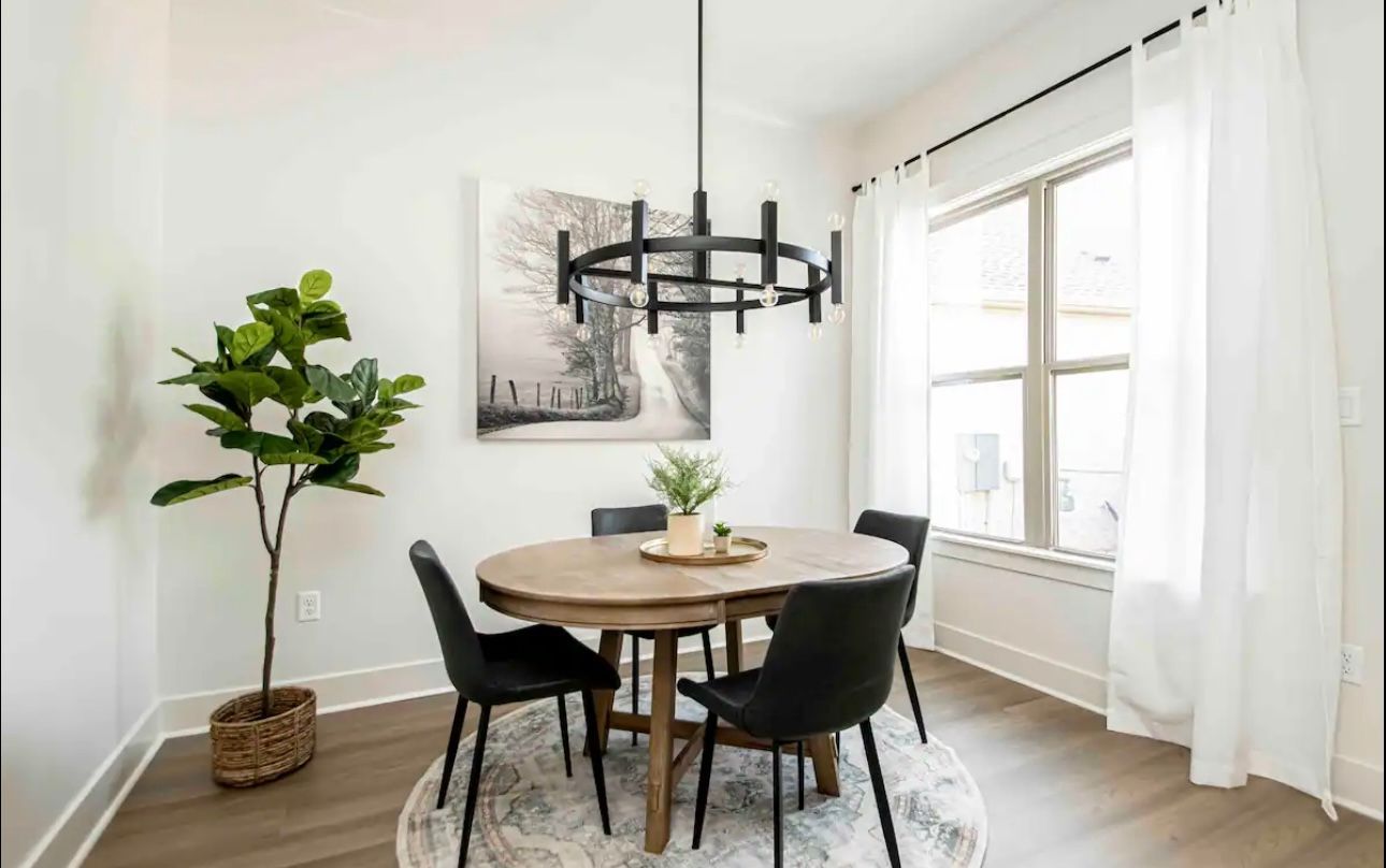Dining room with round wooden table, four black chairs, and a modern chandelier.