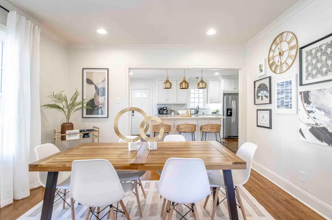 Dining room with wooden table, white chairs, and gallery wall. View to kitchen with pendant lights.
