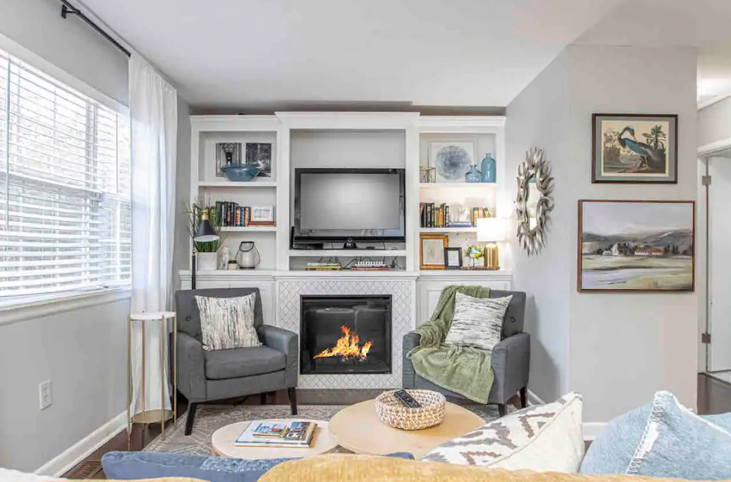 Living room with fireplace, built-in shelves, TV, two armchairs, and round coffee table.