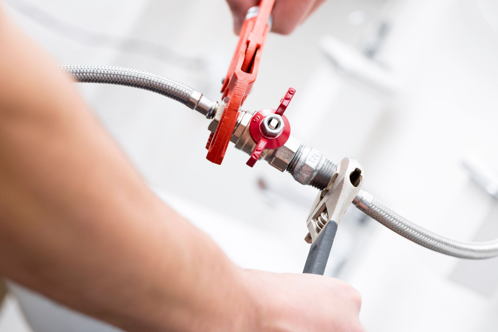Worker tightening a silver pipe fitting with a red clamp tool