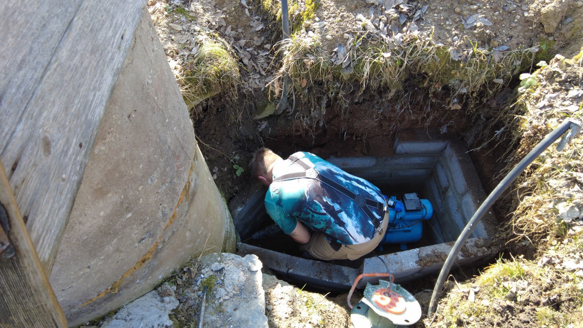 Worker in blue jacket in a narrow underground excavation beside concrete walls and a bucket. Worker in blue jacket in a narrow underground excavation beside concrete walls and a bucket.