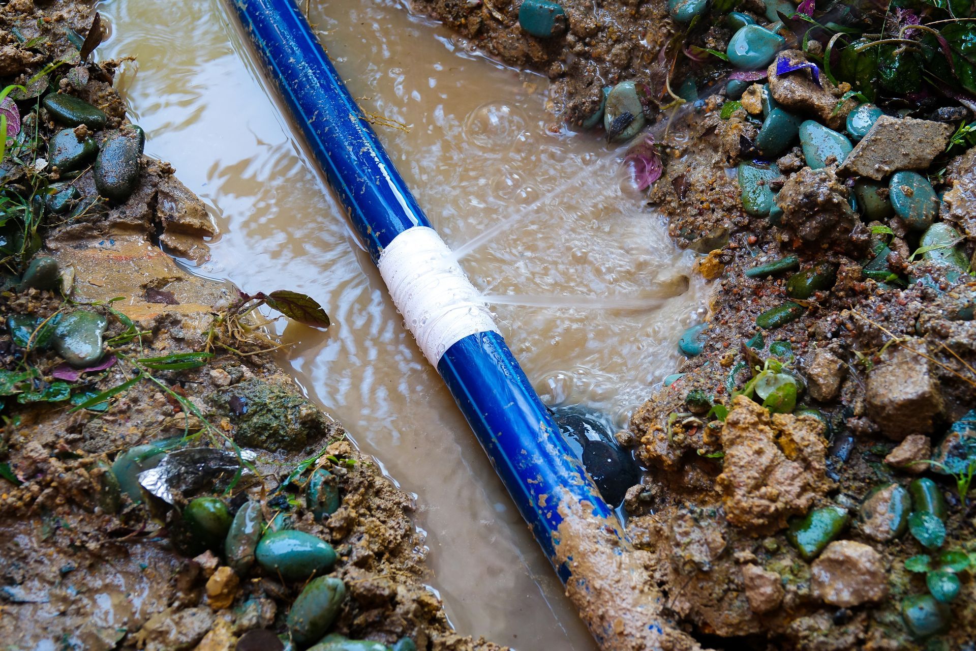 Blue pipe crossing a muddy stream between piles of green and brown rocks
