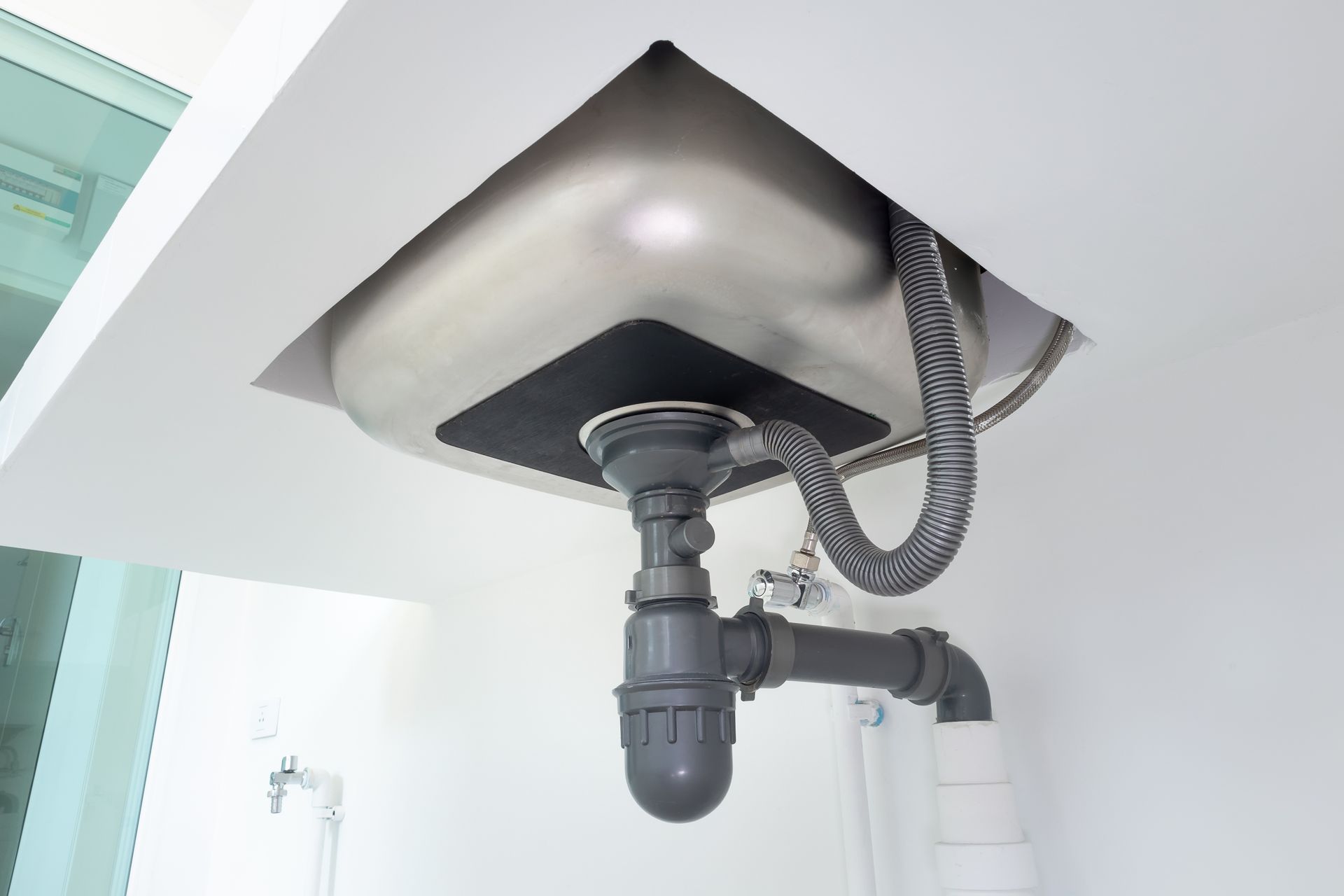 Under-sink plumbing and drain trap beneath a white sink basin