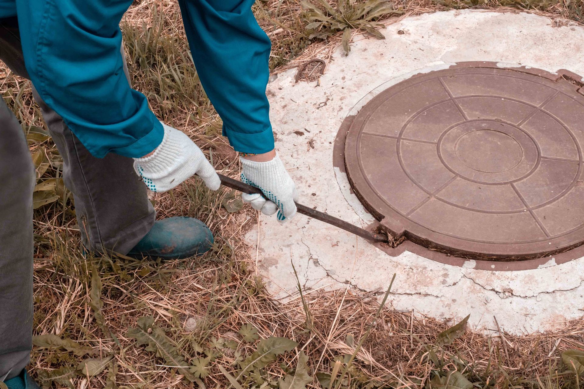 Technician using a pry bar to lift a septic tank lid during septic system service in Lancaster, VA Technician using a pry bar to lift a septic tank lid during septic system service in Lancaster, VA