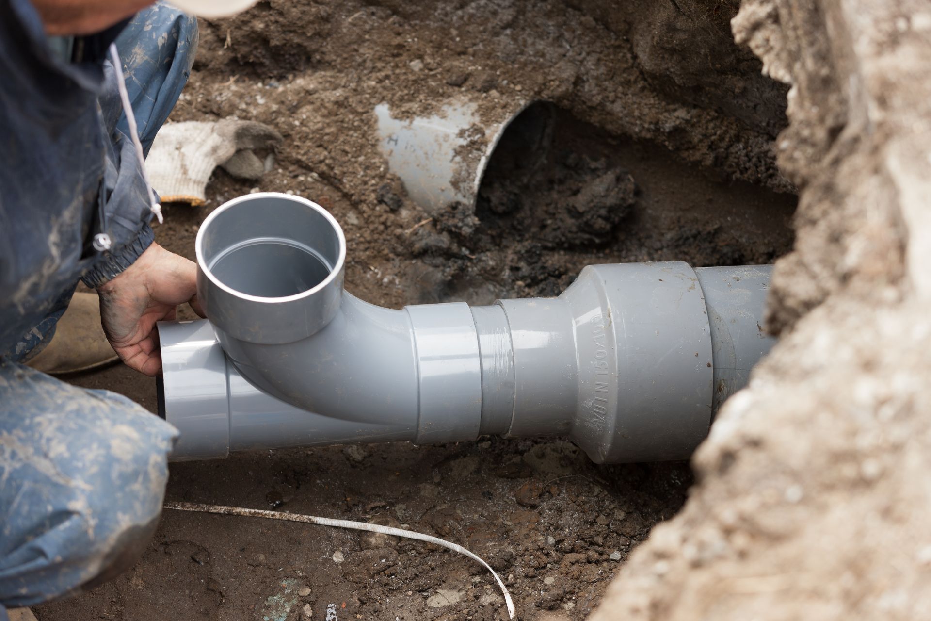 Worker installing gray PVC pipe in a trench underground Worker installing gray PVC pipe in a trench underground