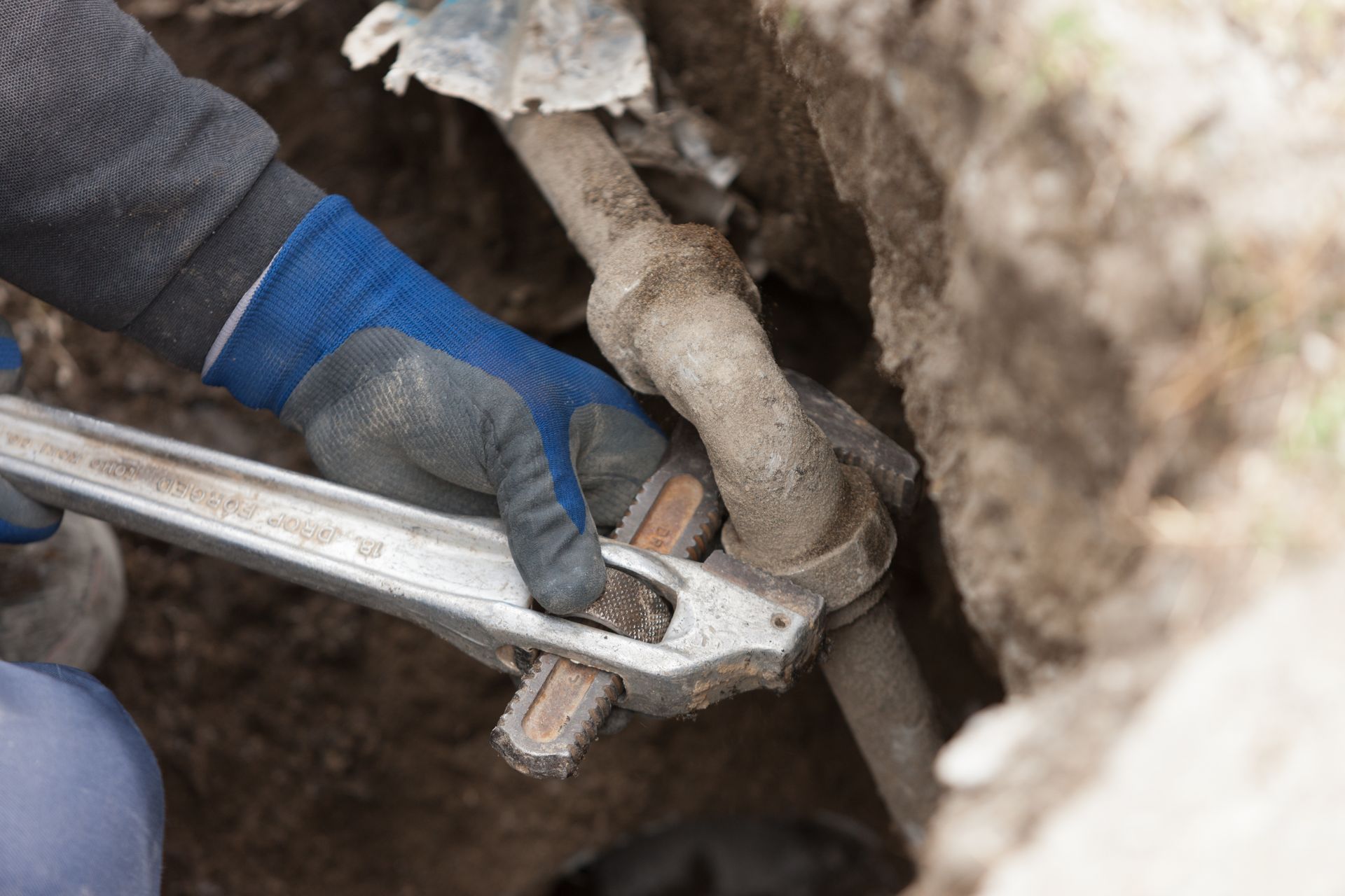 Gloved hands use a wrench to tighten a pipe fitting in a dirt trench. Gloved hands use a wrench to tighten a pipe fitting in a dirt trench.