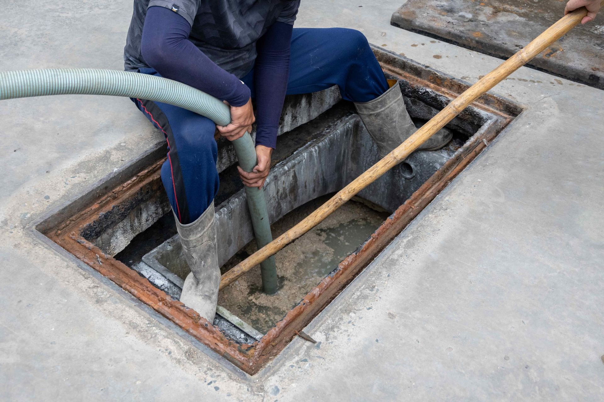 Worker cleaning a manhole with a hose and long pole on a concrete surface Worker cleaning a manhole with a hose and long pole on a concrete surface