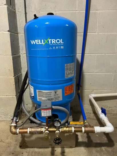 Blue Welltrol pressure tank with connected pipes and valves in a utility room