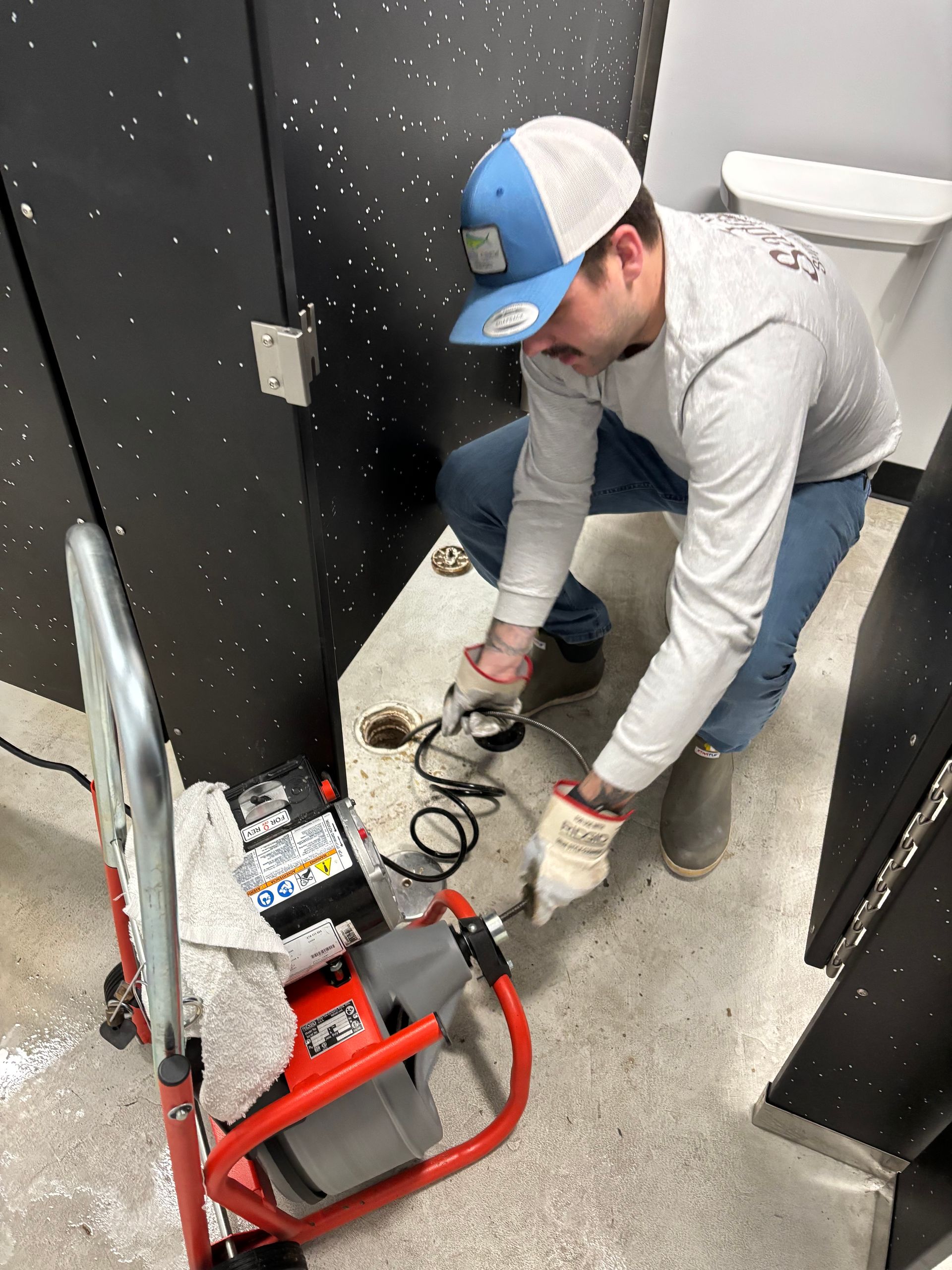 Person kneeling by a wall, using tools to work on a bathroom toilet area.