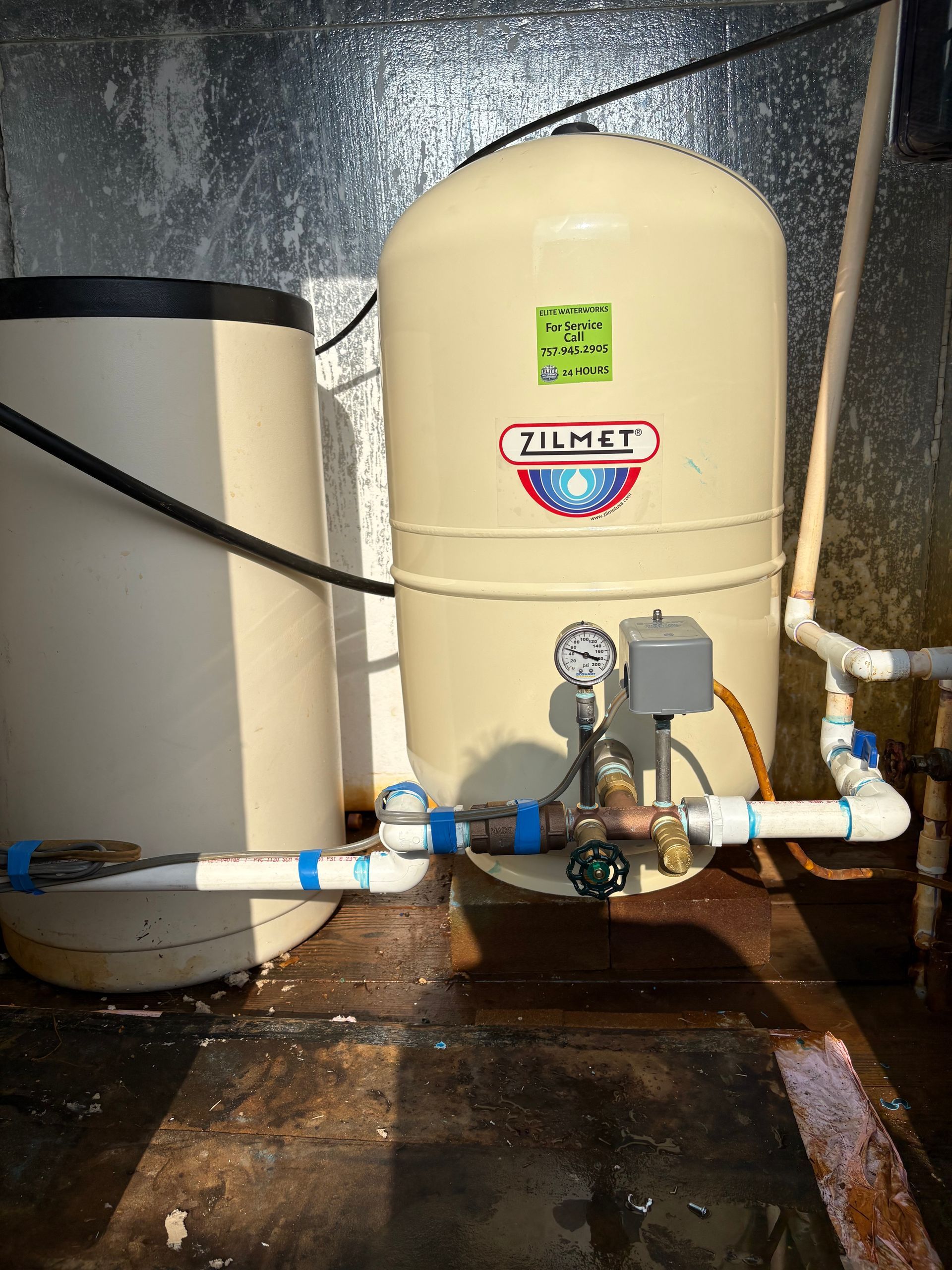 Two beige water storage tanks with connected pipes in a damp utility room Two beige water storage tanks with connected pipes in a damp utility room