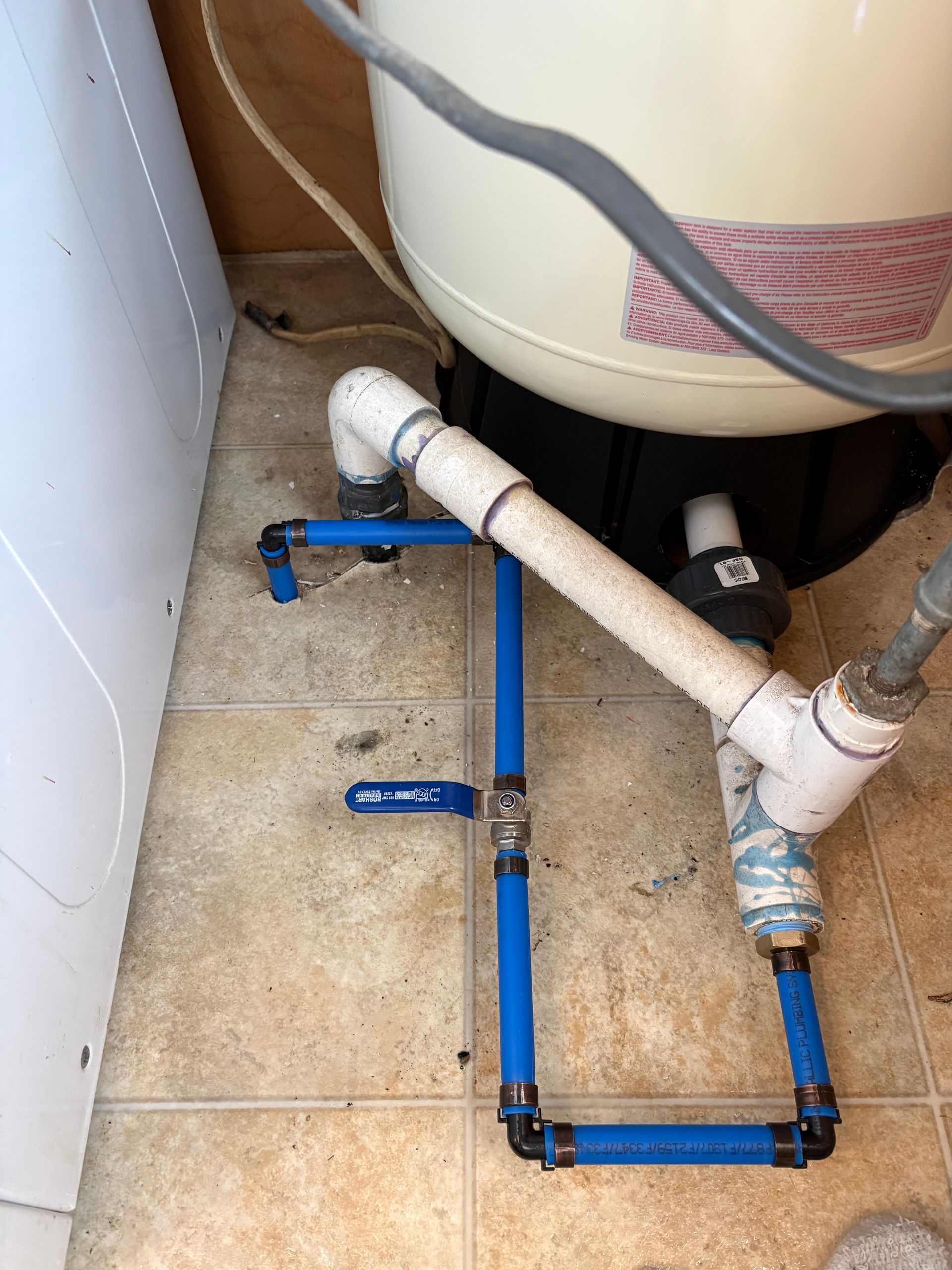 Blue PVC pipes and valves connected under a sink next to a white water heater.