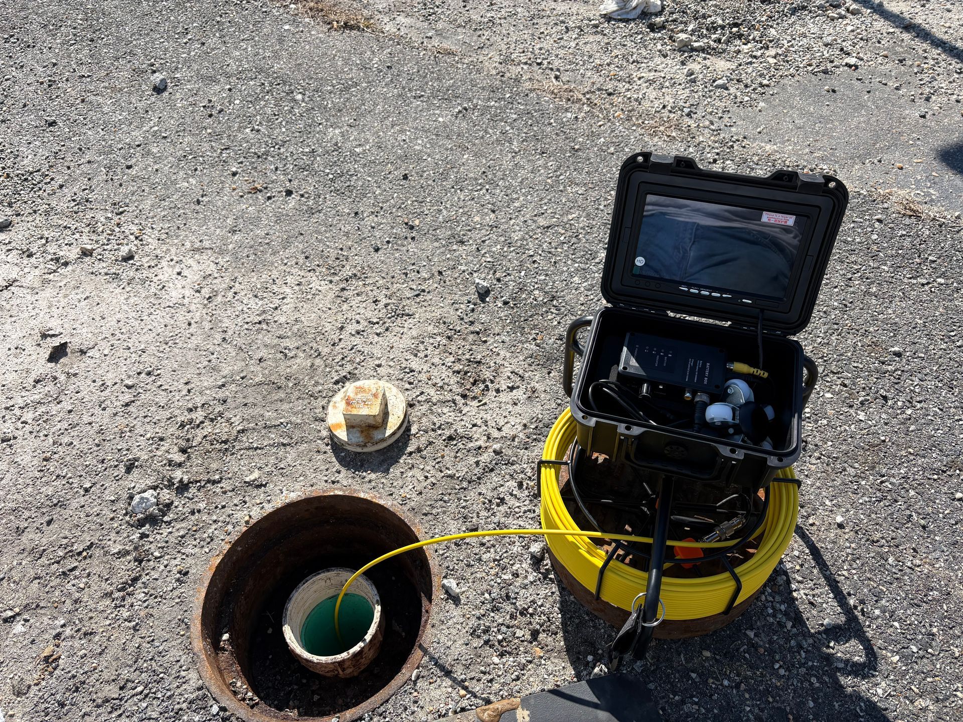 Inspection camera setup beside an open pipe on gravel, with a yellow unit and monitor open. Inspection camera setup beside an open pipe on gravel, with a yellow unit and monitor open.