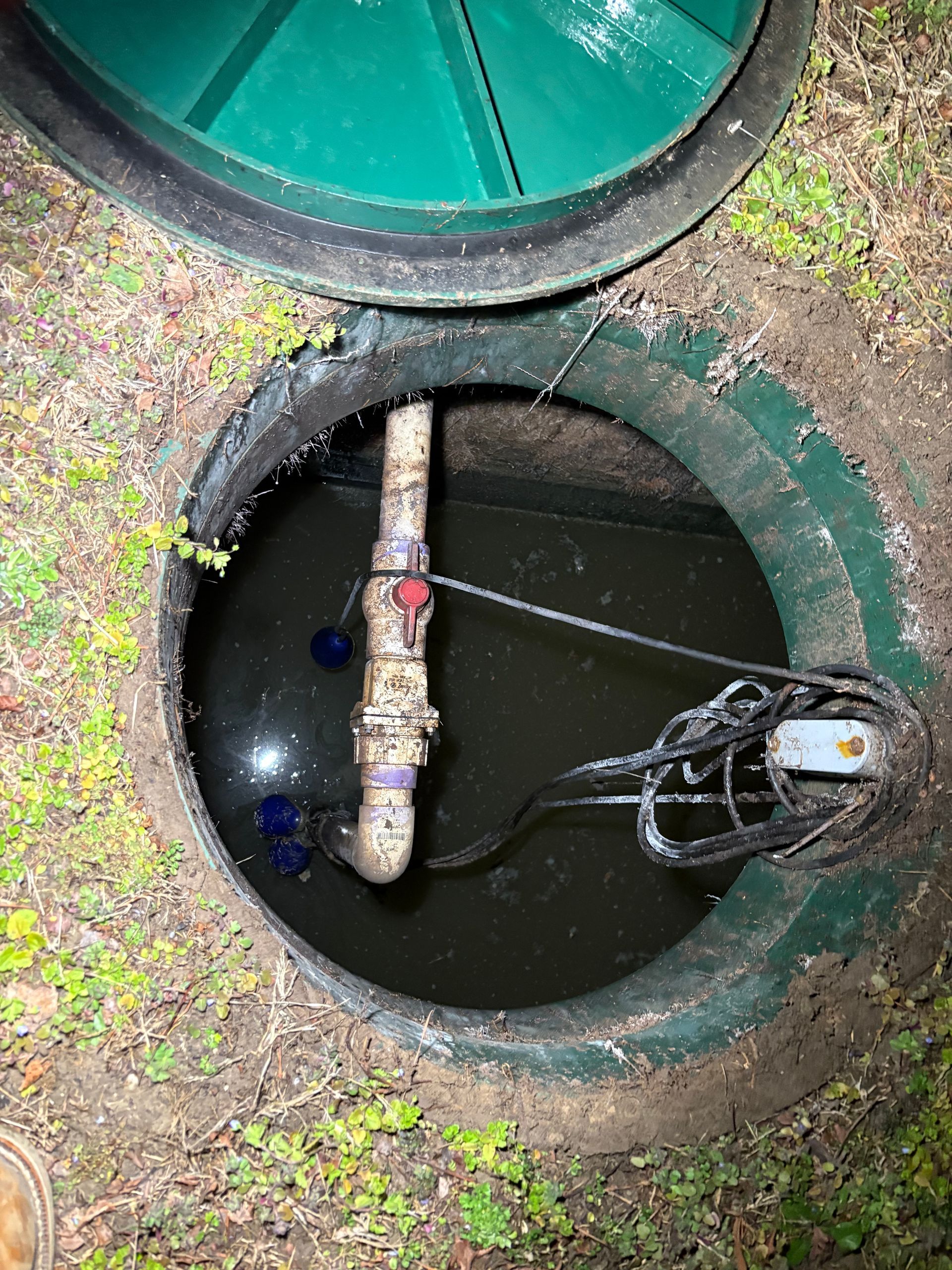 Open utility manhole with dark water, pipes, and a valve visible inside.